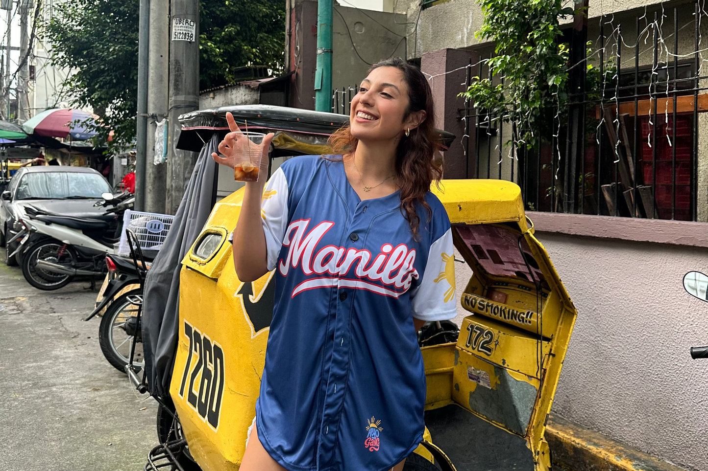 HeyoLeah in a blue 'Manila' jersey standing next to a yellow rickshaw on a street.